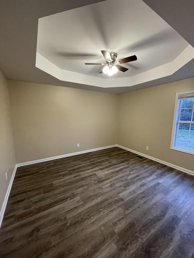 unfurnished room featuring dark hardwood / wood-style flooring, ceiling fan, and a raised ceiling