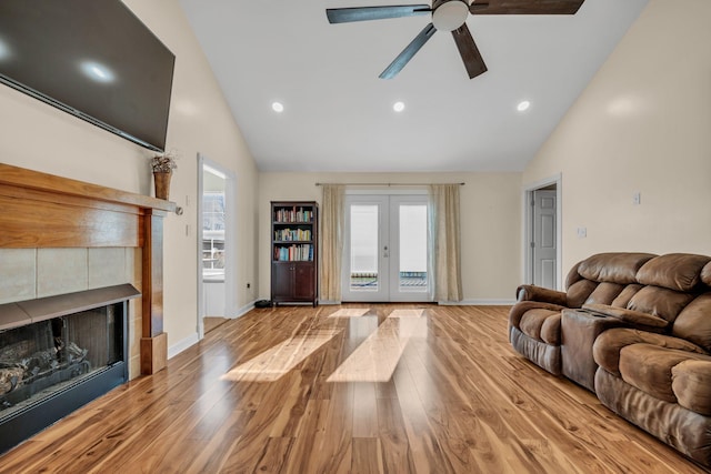 living room with high vaulted ceiling, a tiled fireplace, ceiling fan, light hardwood / wood-style floors, and french doors