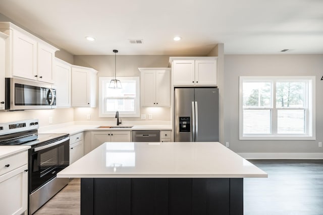 kitchen with appliances with stainless steel finishes, sink, white cabinets, a center island, and hanging light fixtures