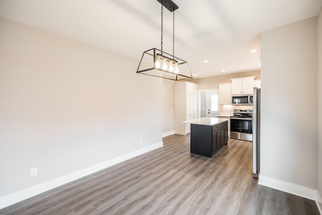 kitchen featuring white cabinetry, a center island, hanging light fixtures, appliances with stainless steel finishes, and light wood-type flooring