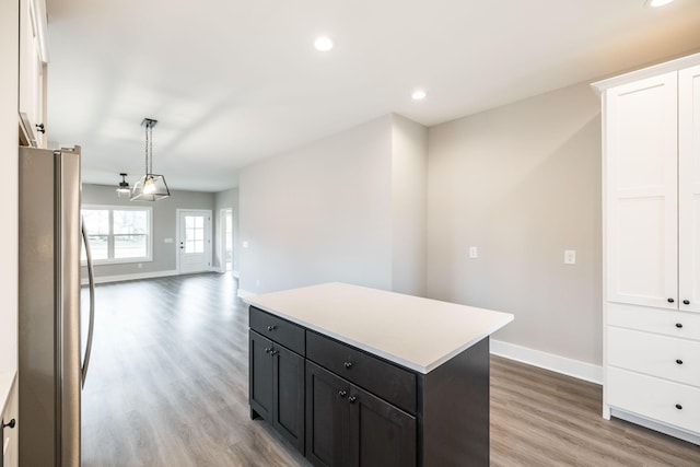 kitchen with light wood-type flooring, decorative light fixtures, a center island, white cabinetry, and stainless steel refrigerator