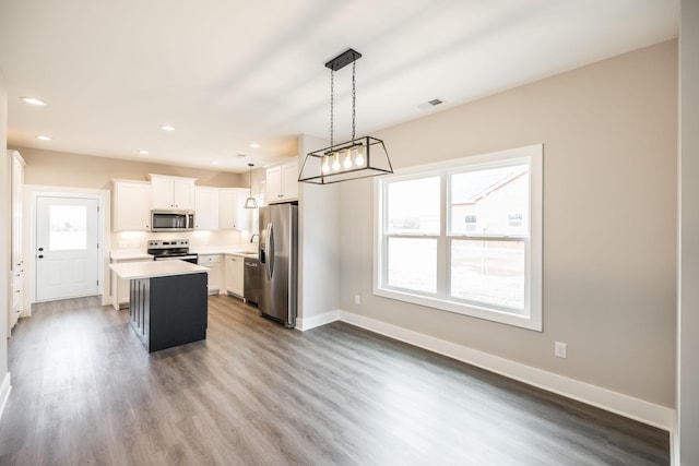 kitchen featuring pendant lighting, a center island, hardwood / wood-style flooring, white cabinetry, and stainless steel appliances