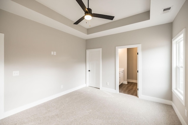 unfurnished bedroom featuring carpet, ceiling fan, a raised ceiling, and ensuite bath