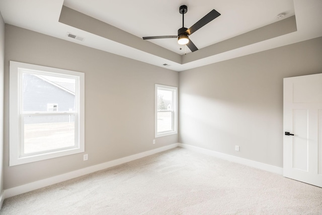 carpeted empty room featuring ceiling fan and a raised ceiling