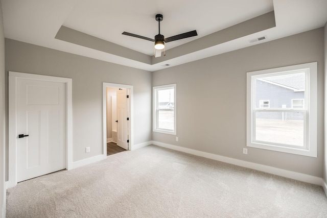 unfurnished bedroom with light carpet, connected bathroom, a tray ceiling, and ceiling fan