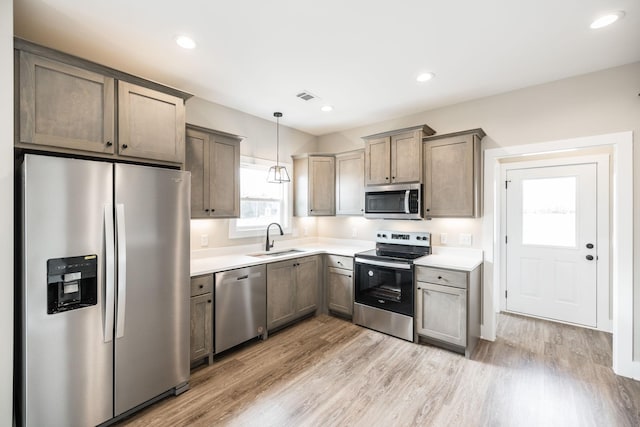 kitchen with decorative light fixtures, sink, stainless steel appliances, and light hardwood / wood-style flooring