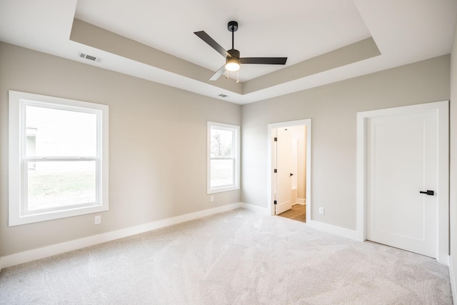 unfurnished bedroom featuring a tray ceiling, ensuite bath, ceiling fan, and multiple windows