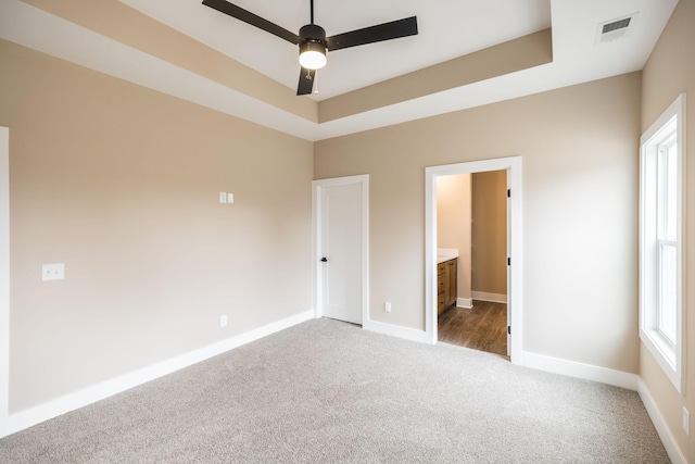 unfurnished bedroom featuring carpet, a tray ceiling, ensuite bath, and ceiling fan