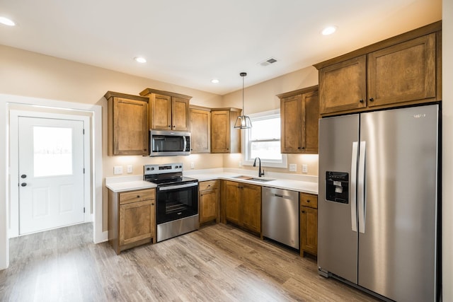 kitchen with hanging light fixtures, sink, stainless steel appliances, and light hardwood / wood-style floors