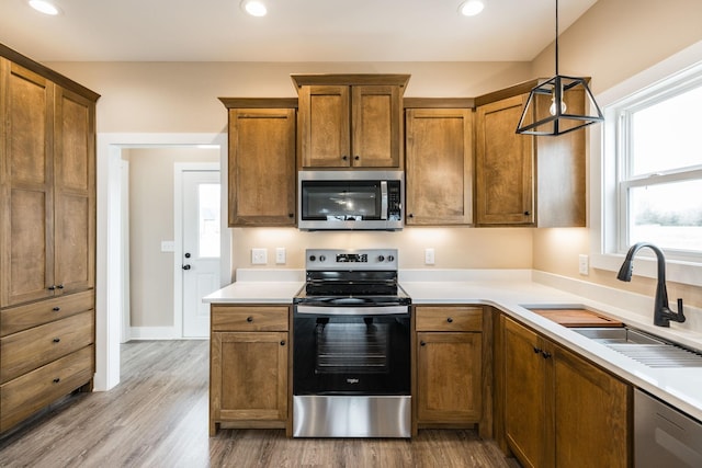 kitchen featuring sink, stainless steel appliances, hanging light fixtures, and light hardwood / wood-style flooring