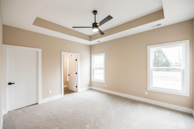 unfurnished bedroom featuring multiple windows, ensuite bath, a raised ceiling, and ceiling fan