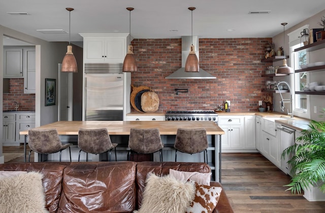 kitchen with white cabinets, wall chimney range hood, appliances with stainless steel finishes, and wooden counters