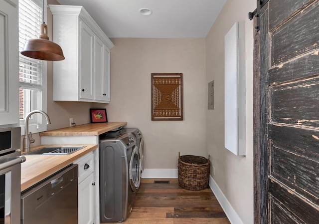 clothes washing area with a barn door, independent washer and dryer, sink, and dark wood-type flooring