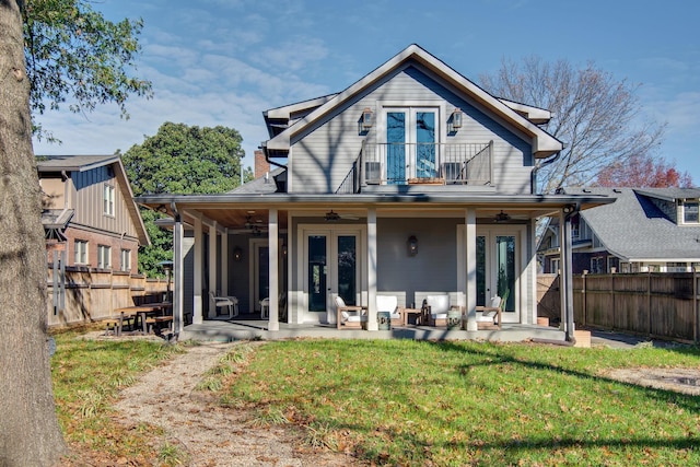 back of property with ceiling fan, a balcony, a yard, and french doors