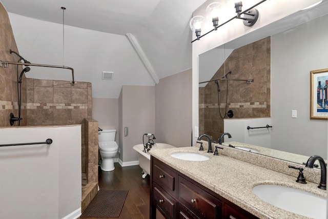 bathroom featuring hardwood / wood-style floors, vanity, lofted ceiling, toilet, and a tile shower