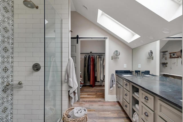 bathroom featuring vaulted ceiling with skylight, vanity, a tile shower, and hardwood / wood-style floors