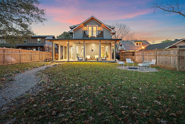 back house at dusk with a lawn, a patio area, ceiling fan, and a balcony