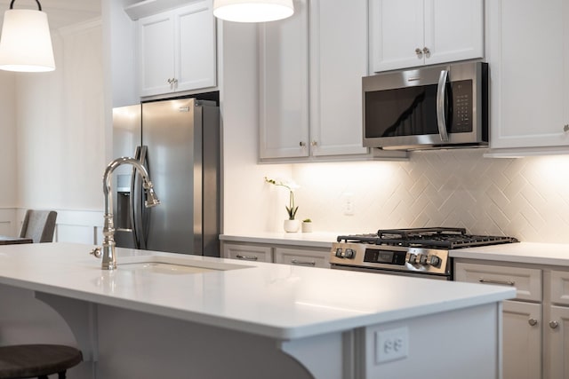 kitchen featuring a kitchen bar, appliances with stainless steel finishes, backsplash, decorative light fixtures, and white cabinetry