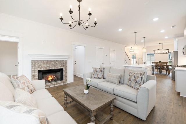 living room featuring a fireplace, dark wood-type flooring, an inviting chandelier, and ornamental molding