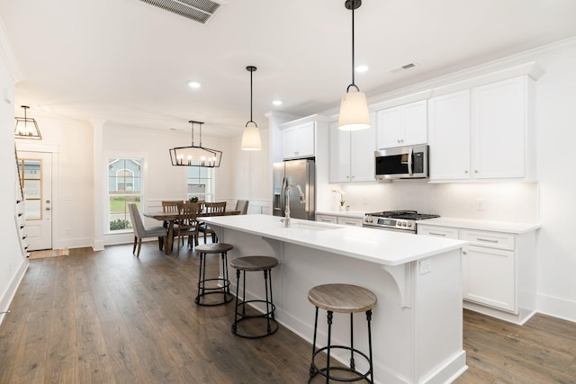 kitchen featuring appliances with stainless steel finishes, pendant lighting, white cabinets, dark hardwood / wood-style floors, and an island with sink