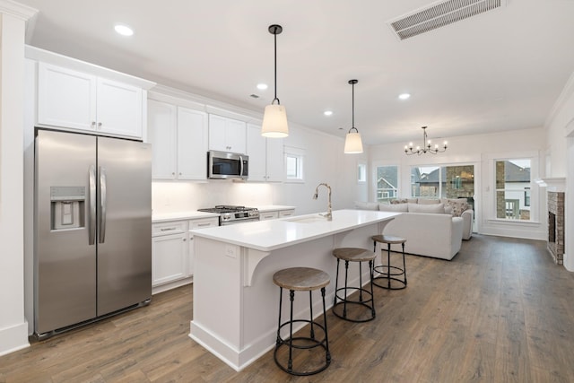 kitchen with sink, stainless steel appliances, pendant lighting, a center island with sink, and white cabinets