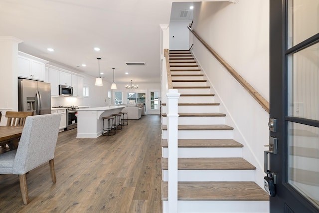 stairway with hardwood / wood-style floors and an inviting chandelier