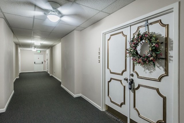 hall with a paneled ceiling and dark carpet