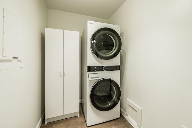 laundry area with cabinets, stacked washing maching and dryer, and electric panel