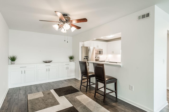 kitchen with a breakfast bar, ceiling fan, appliances with stainless steel finishes, dark hardwood / wood-style flooring, and white cabinetry