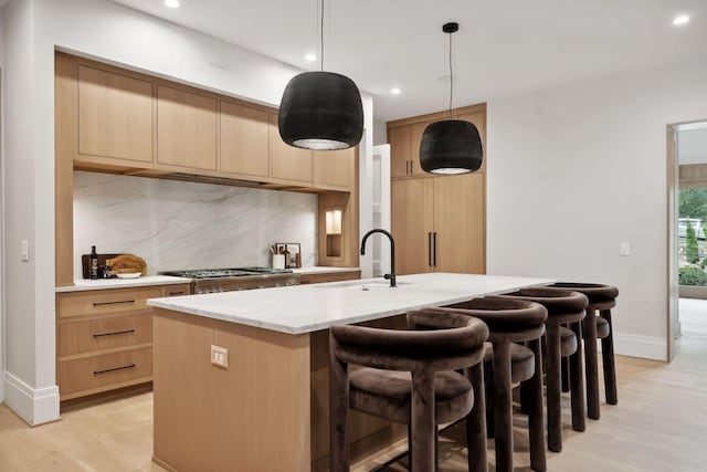 kitchen with decorative light fixtures, sink, an island with sink, and light brown cabinetry