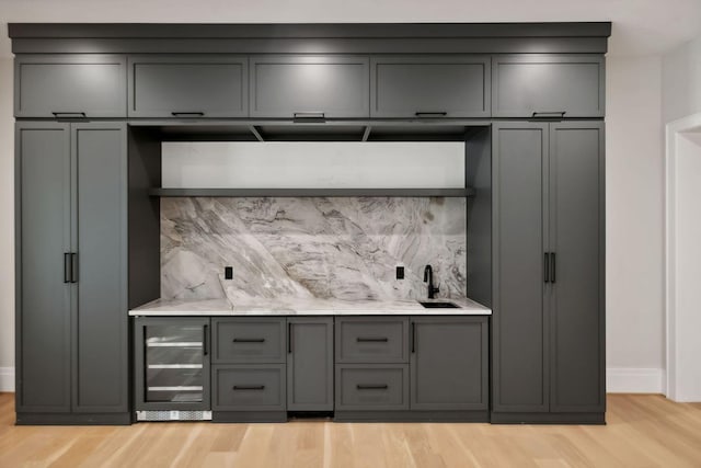 bar with light wood-type flooring, backsplash, sink, gray cabinets, and wine cooler