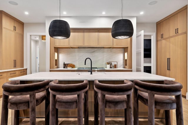 kitchen featuring tasteful backsplash, light brown cabinets, pendant lighting, and a center island with sink