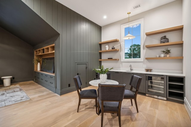 dining space with wood walls, sink, beverage cooler, and light wood-type flooring