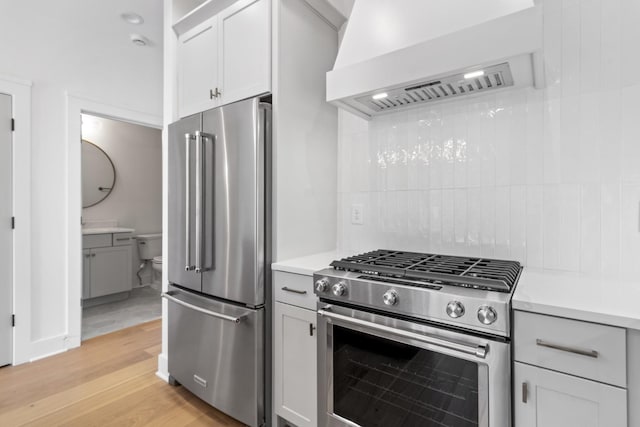 kitchen with white cabinetry, high end appliances, light hardwood / wood-style floors, premium range hood, and backsplash