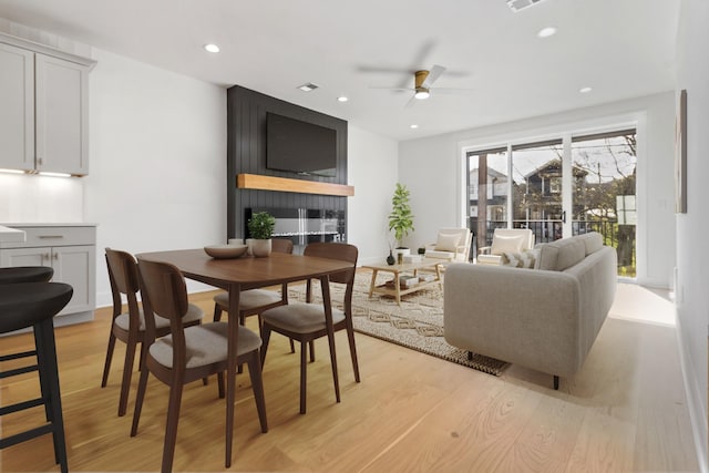 living room featuring ceiling fan, light hardwood / wood-style flooring, and a fireplace