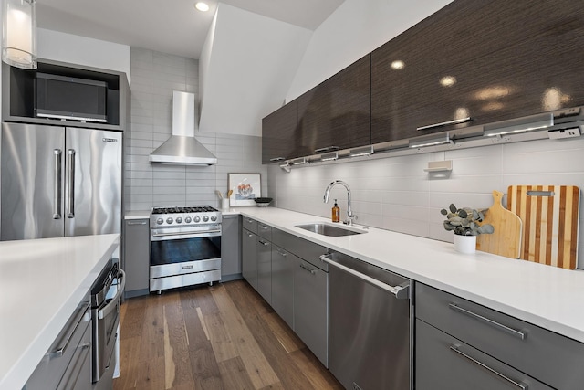 kitchen with decorative backsplash, high end appliances, sink, wall chimney range hood, and dark hardwood / wood-style floors