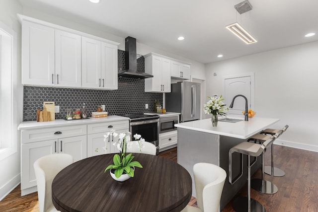 kitchen featuring appliances with stainless steel finishes, an island with sink, white cabinets, backsplash, and wall chimney exhaust hood