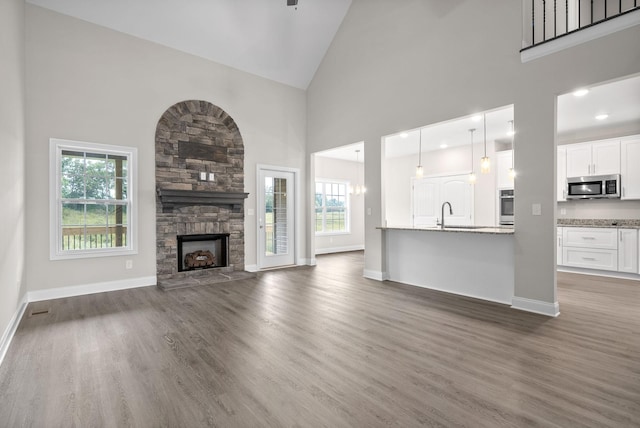 unfurnished living room with dark wood-type flooring, plenty of natural light, a stone fireplace, and high vaulted ceiling