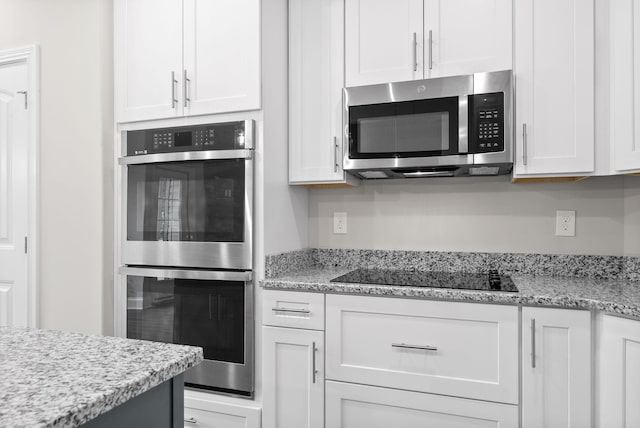 kitchen with stainless steel appliances, white cabinetry, and light stone counters