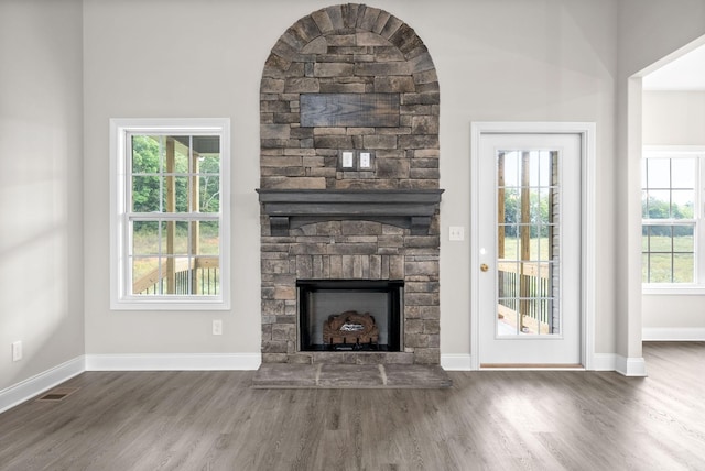 unfurnished living room featuring dark hardwood / wood-style flooring, a wealth of natural light, and a stone fireplace