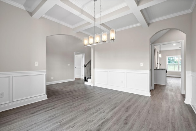 unfurnished dining area featuring coffered ceiling, wood-type flooring, a chandelier, crown molding, and beam ceiling