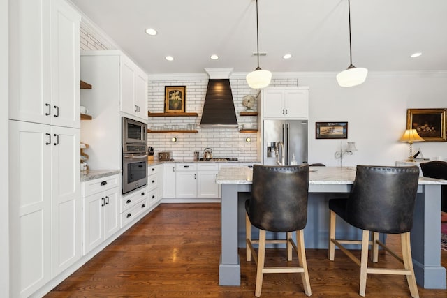 kitchen with light stone countertops, appliances with stainless steel finishes, custom range hood, decorative light fixtures, and white cabinets