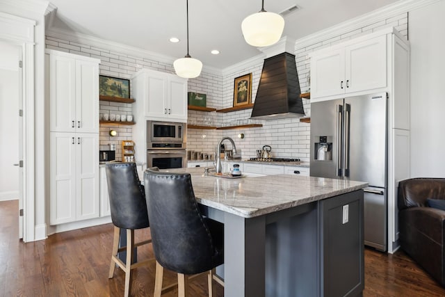 kitchen with appliances with stainless steel finishes, backsplash, light stone counters, a center island with sink, and white cabinetry