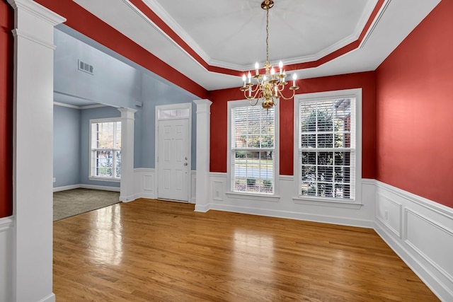 unfurnished dining area with a healthy amount of sunlight, ornamental molding, decorative columns, a tray ceiling, and hardwood / wood-style flooring