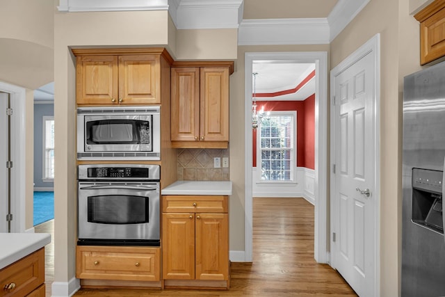 kitchen featuring an inviting chandelier, light hardwood / wood-style flooring, backsplash, appliances with stainless steel finishes, and ornamental molding