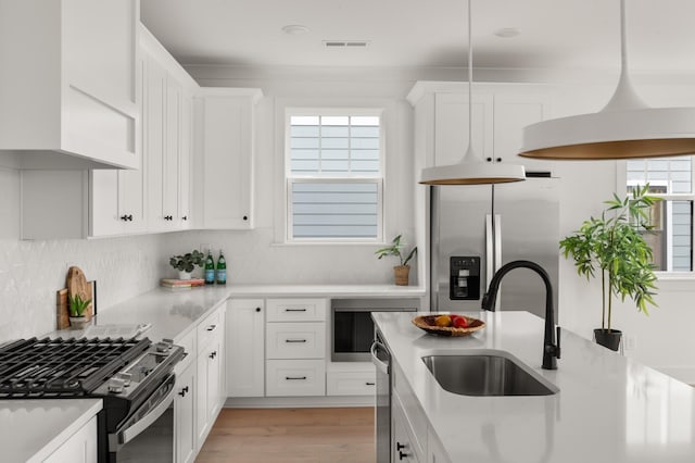 kitchen with white cabinetry, sink, hanging light fixtures, backsplash, and appliances with stainless steel finishes