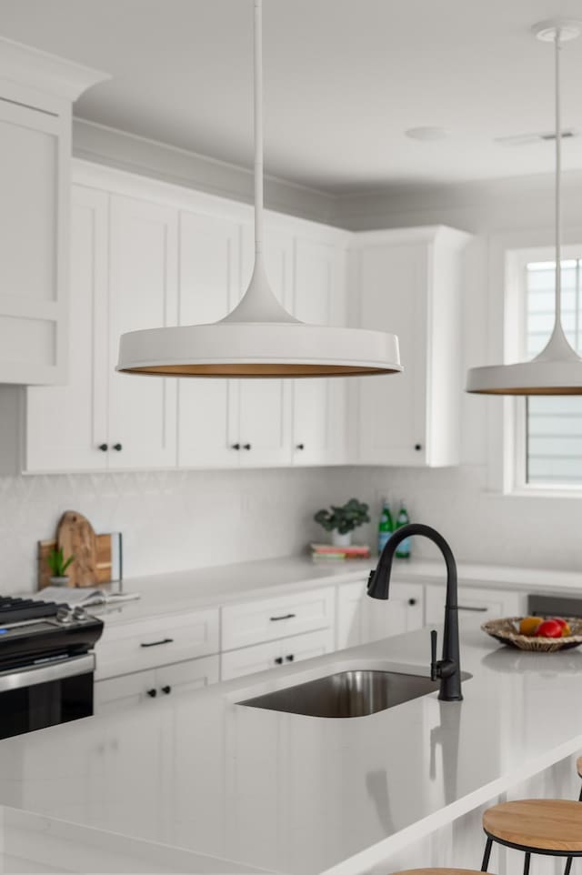 kitchen with a kitchen breakfast bar, backsplash, sink, white cabinets, and hanging light fixtures