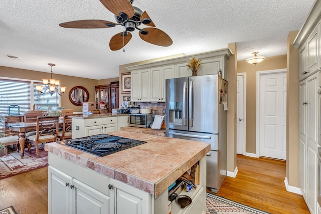 kitchen with ceiling fan with notable chandelier, stainless steel appliances, decorative light fixtures, and a kitchen island