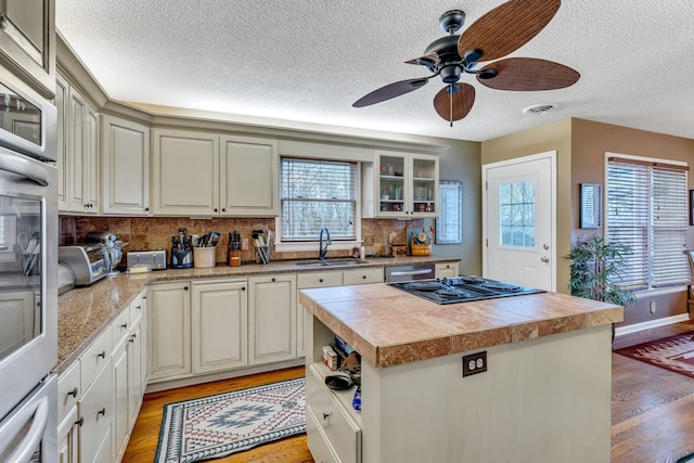 kitchen featuring dishwasher, sink, decorative backsplash, a kitchen island, and gas cooktop