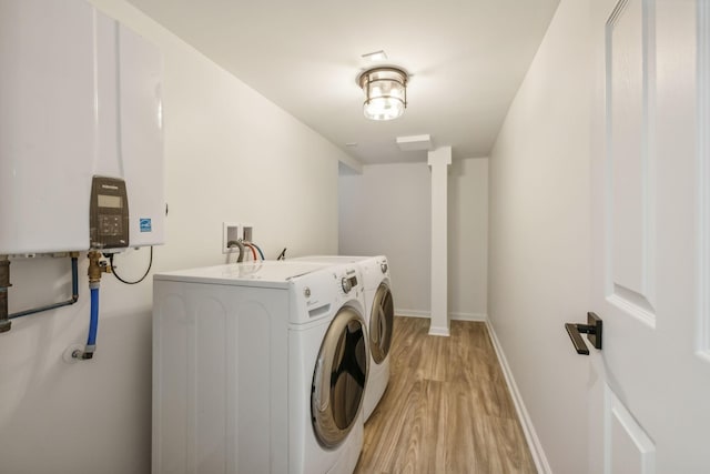 clothes washing area featuring light wood-type flooring, washing machine and dryer, and water heater